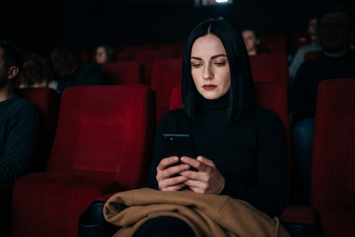 Ghosting – kobieta siedzi w sali kinowej obok pustego fotela i patrzy w telefon zamiast na ekran